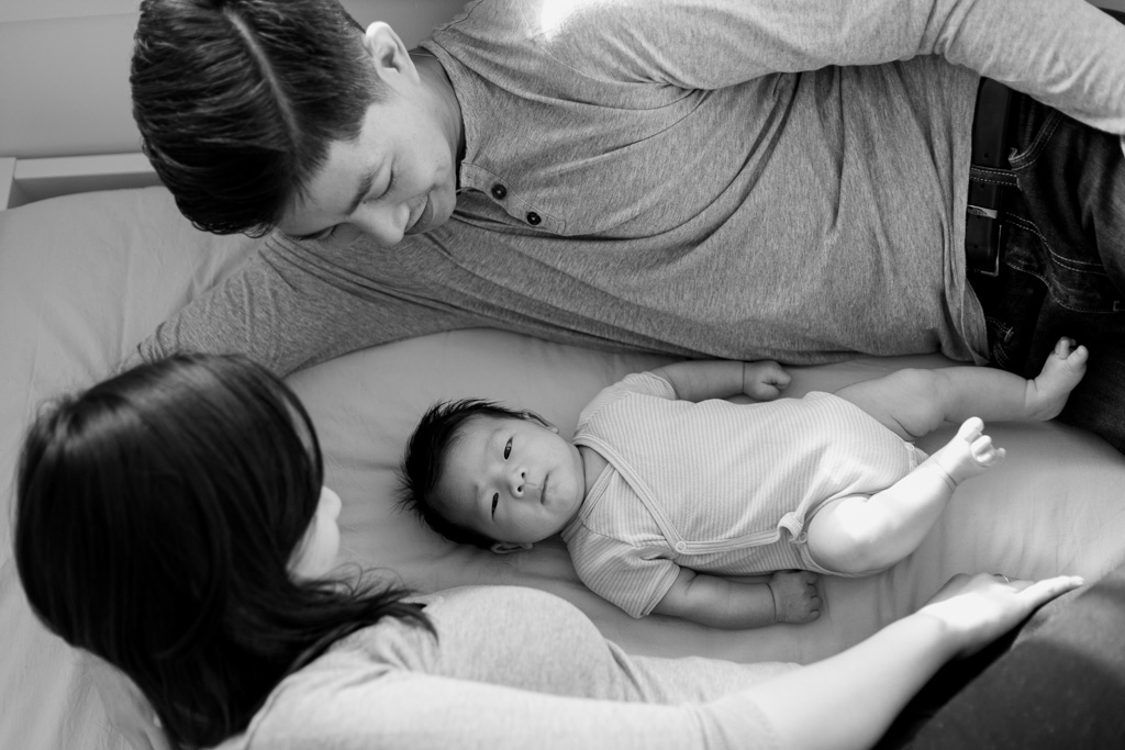 Parents allongés au lit avec bébé qui regarde l’appareil photo