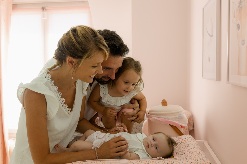 Parents et aînée regardant bébé de 3 mois sur la table à langer, photographe naissance à domicile Vincennes
