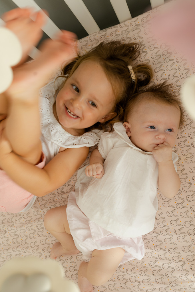 Aînée jouant avec sa petite sœur dans le berceau, photographe naissance à domicile Noisy-le-Grand