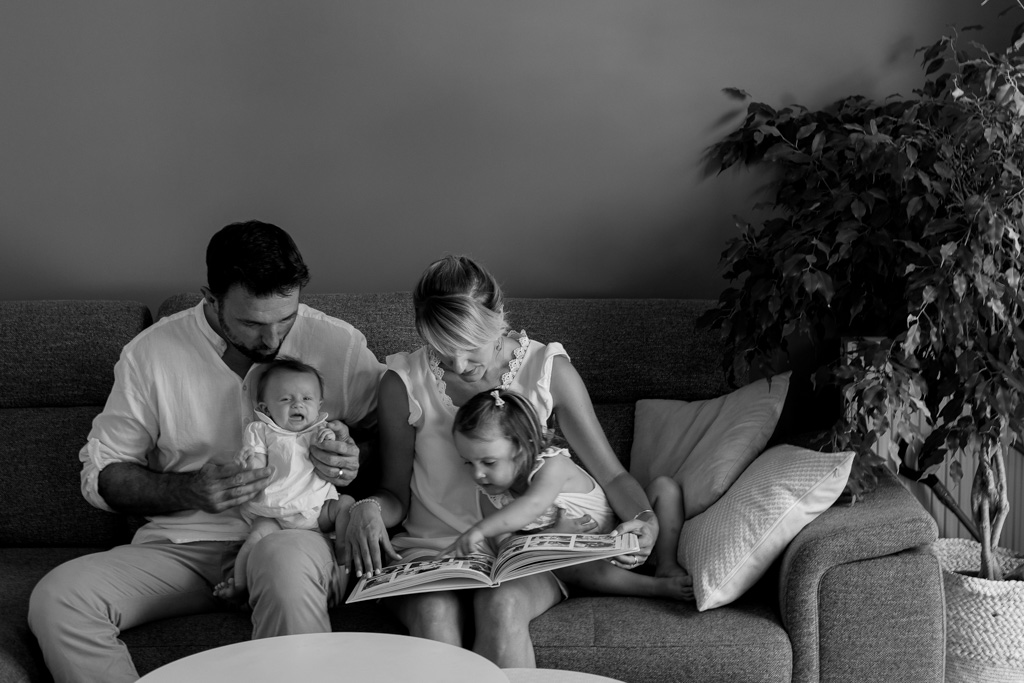 Famille avec nouveau-né et parents montrant l’album photo à l’aînée, photographe naissance à domicile Paris