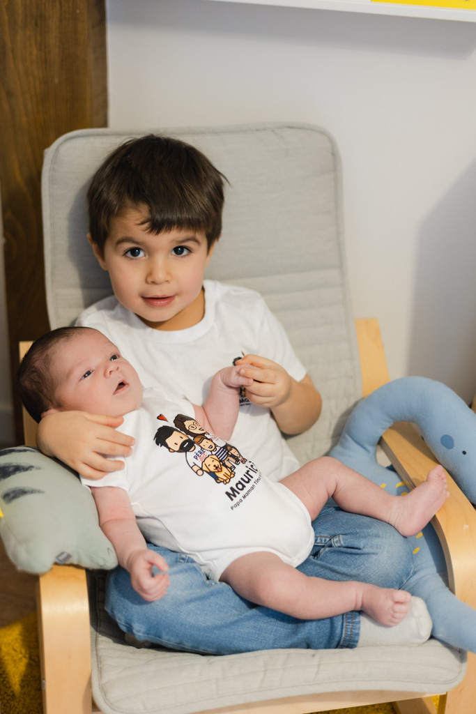 L’aîné tient délicatement le nouveau-né dans ses bras, séance naissance à domicile à Saint-Maur