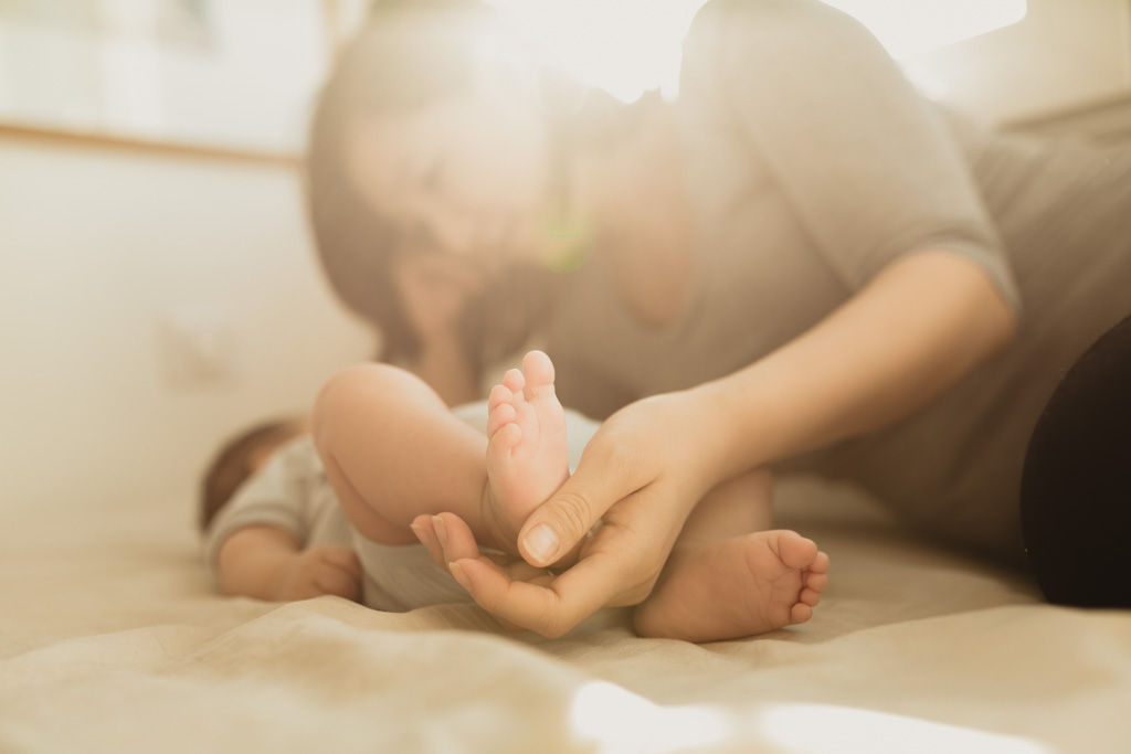 Photo rapprochée de bébé à domicile : maman tient le bébé, papa pose ses mains sur sa tête, les mains des parents illustrant la petite taille du bébé, séance naissance à Vincennes