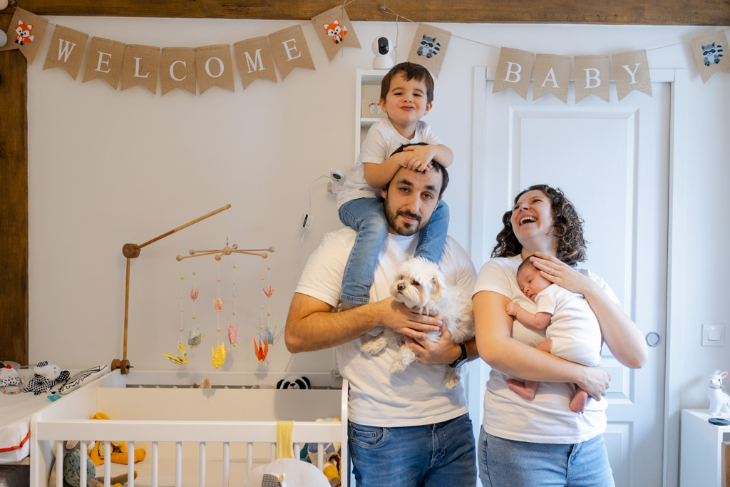 Famille réunie dans la chambre du bébé : maman avec son nouveau-né, papa avec le chien et l’aîné, moment joyeux et naturel capturé à domicile à Villejuif, en région parisienne