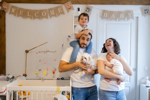 Famille réunie dans la chambre du bébé : maman avec son nouveau-né, papa avec le chien et l’aîné, moment joyeux et naturel capturé à domicile à Villejuif, en région parisienne