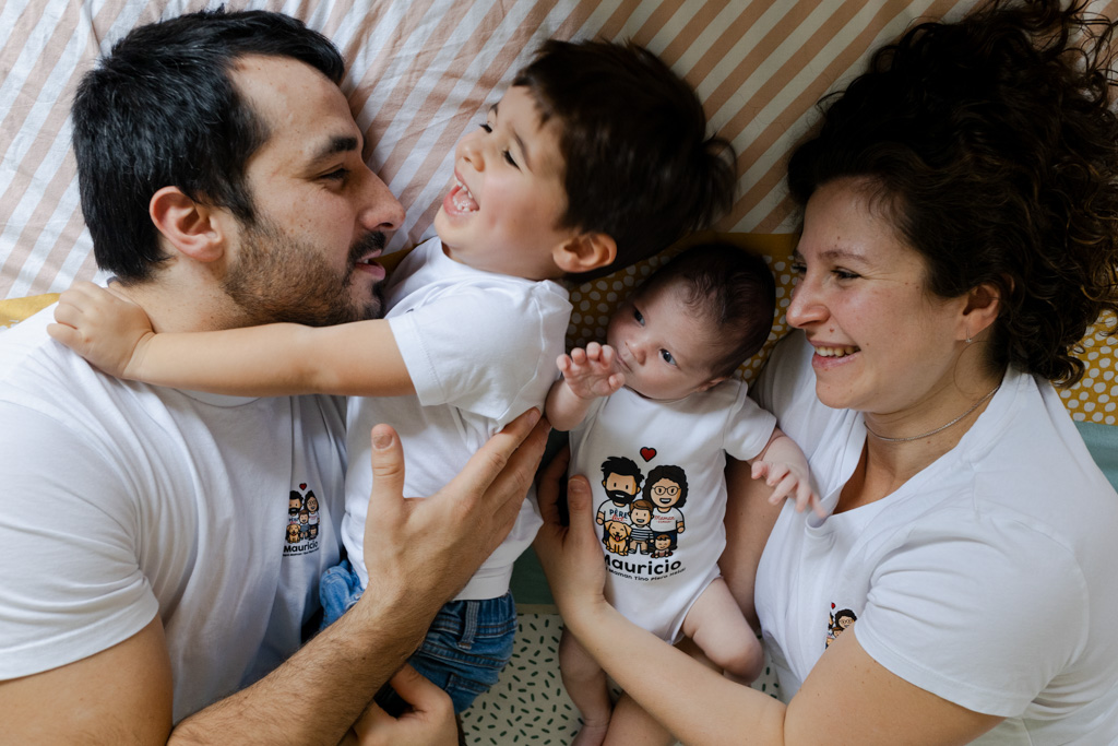 Famille heureuse allongée sur le lit avec bébé et aîné, séance photo à domicile à Villejuif