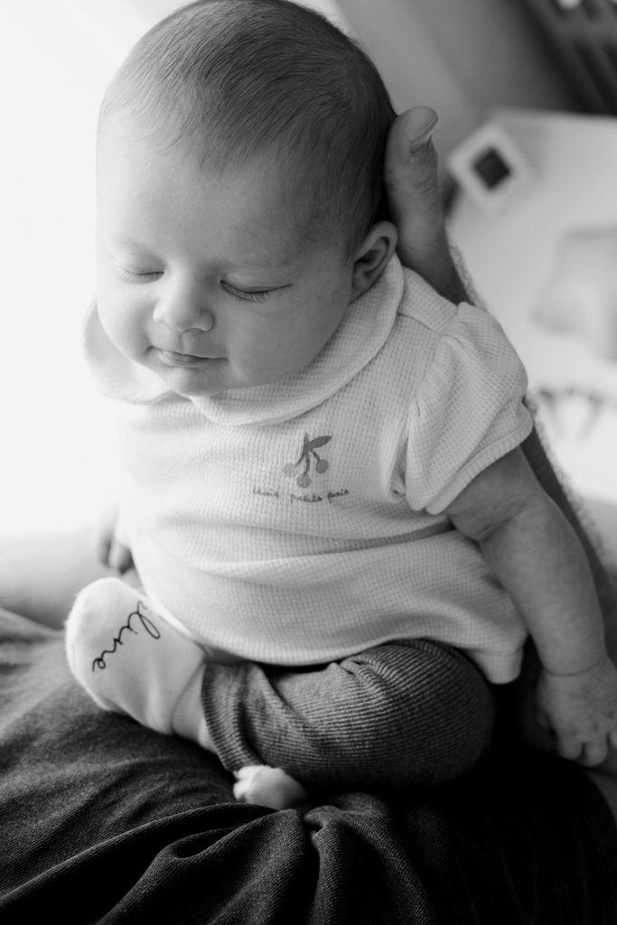 Photo rapprochée d’un bébé souriant dans les bras de sa maman à domicile, photographe naissance Saint-Maur