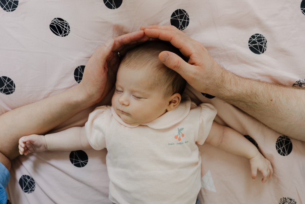Les mains des parents entourent la tête du bébé, symbole de protection, séance naissance à domicile à Saint-Maur
