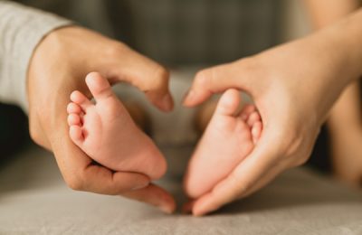 Photo artistique à domicile : les mains des parents forment un cœur autour des petits pieds du bébé, séance naissance à Paris