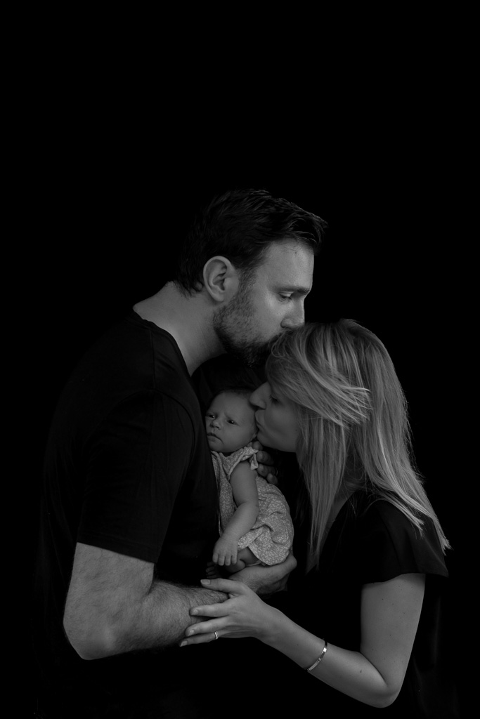 Papa et maman faisant un bisou sur le front du bébé