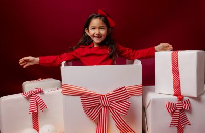 Fille sortant d’une grande boîte cadeau, décor de Noël rouge avec paquets blancs en studio photo à Saint-Maur