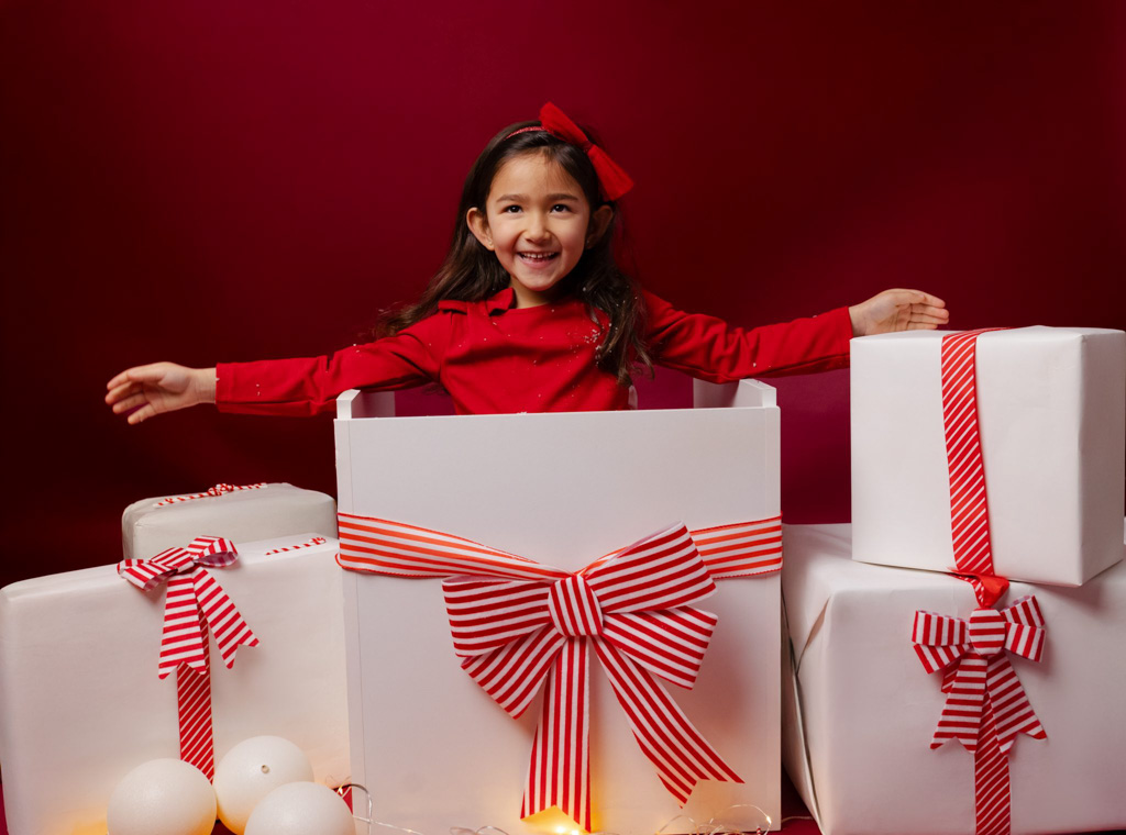 Fille sortant d’une grande boîte cadeau, décor de Noël rouge avec paquets blancs en studio photo à Saint-Maur