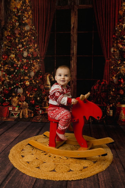 Enfant sur un renne de Noël à bascule devant un décor de sapins dans studio photo à Saint-Maur