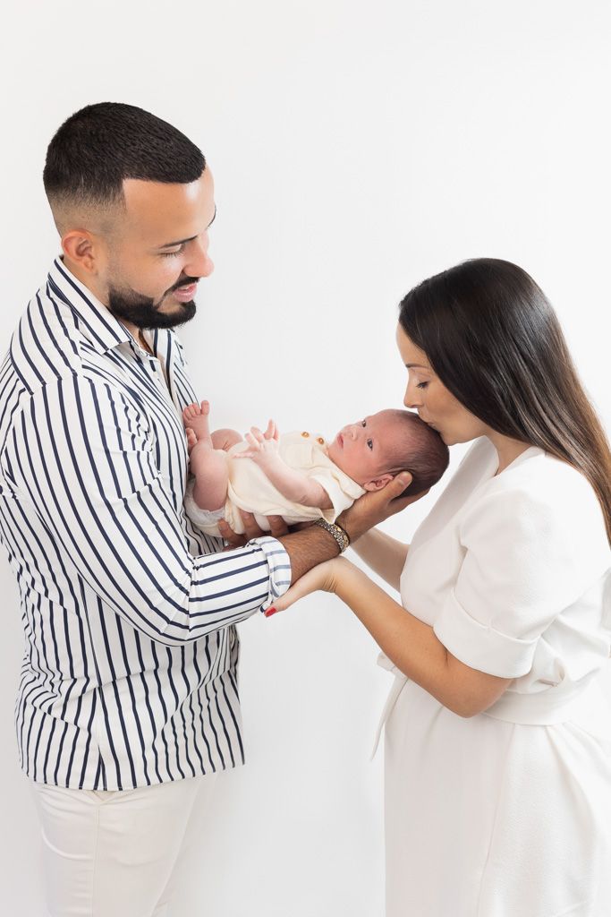 Papa tenant bébé, maman fait un bisou sur le front du bébé