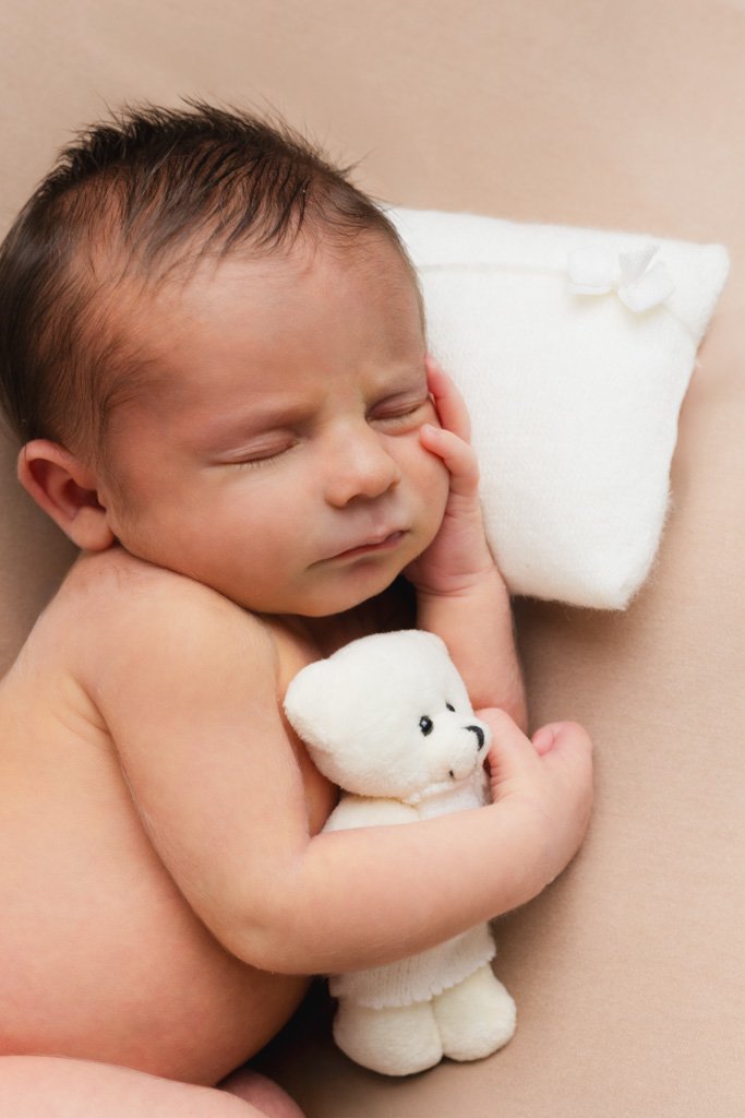 Nouveau-né de 14 jours tenant un doudou, allongé sur un petit oreiller en studio.