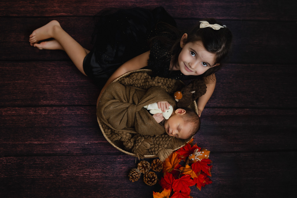 Nouveau-né emmailloté avec sa grande sœur dans un décor automne, studio Saint-Maur